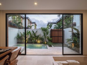 A modern outdoor patio with a swimming pool, surrounded by lush tropical plants and a wooden fence. - La Finca Bingin (Pecatu)