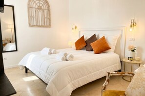 A neatly made bed with pillows, a bedside table with a lamp, and a wall-mounted light fixture.