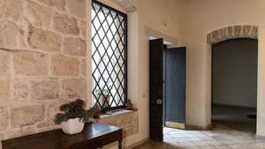 A room with a stone wall, a wooden table with a potted plant, a window with a metal grille, and a dark door leading to another room. - Tresca Charme - Suite 11 Elegant Stay in the Heart of Bari (Bari)