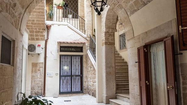 A narrow stone corridor with a staircase leading to a balcony, a door with a patterned design, and a hanging light fixture. - Tresca Charme - Suite 11 Elegant Stay in the Heart of Bari (Bari)