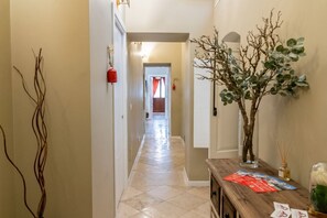 A hallway with a tiled floor, a wooden console table with a vase and a red object, and a wall-mounted decorative piece. - Tresca Charme - Suite 11 Elegant Stay in the Heart of Bari (Bari)