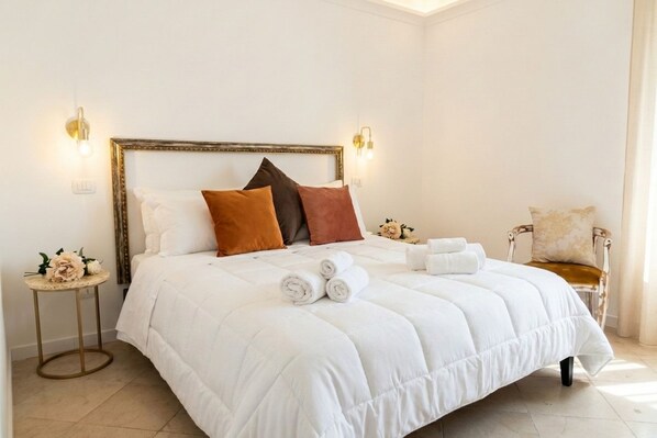 A neatly made bed with a white duvet, brown and white pillows, and rolled towels on a white headboard.