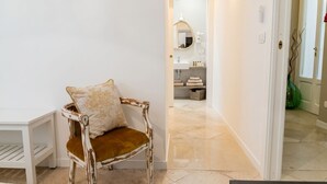 A hallway with a white door, a chair with a cushion, and a bathroom visible in the background.