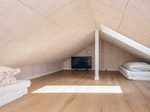 A spacious attic room with a sloped ceiling, a flat-screen TV, a bed with a white comforter, and a wooden floor. - 5 Star Holiday Home in Jerup (Jerup)