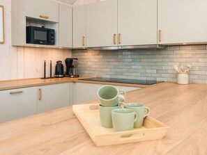 A modern kitchen with light-colored cabinets, a microwave, a coffee maker, and a tray with mugs. - 5 Star Holiday Home in Jerup (Jerup)