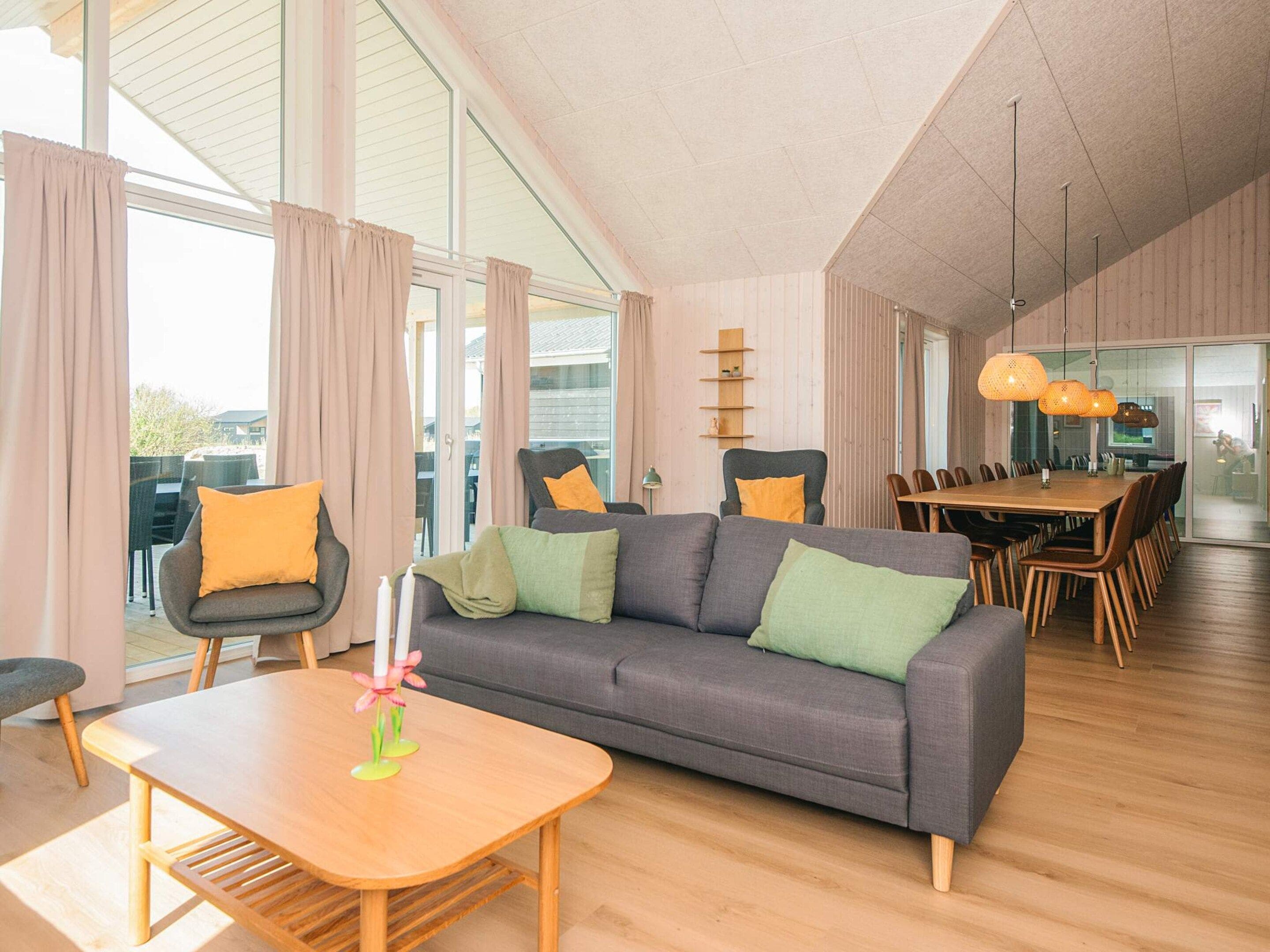 A modern living room with a sofa, chairs, a dining table, and a large window.