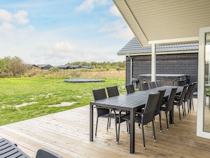 An outdoor deck with a dining table and chairs, a grill, and a trampoline in the background. - 5 Star Holiday Home in Jerup (Jerup)