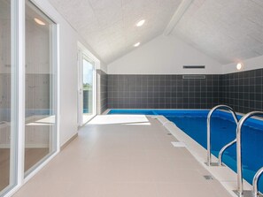 Une piscine intérieure dotée de portes en verre transparent, d’un sol carrelé et d’un plafond équipé de luminaires encastrés.