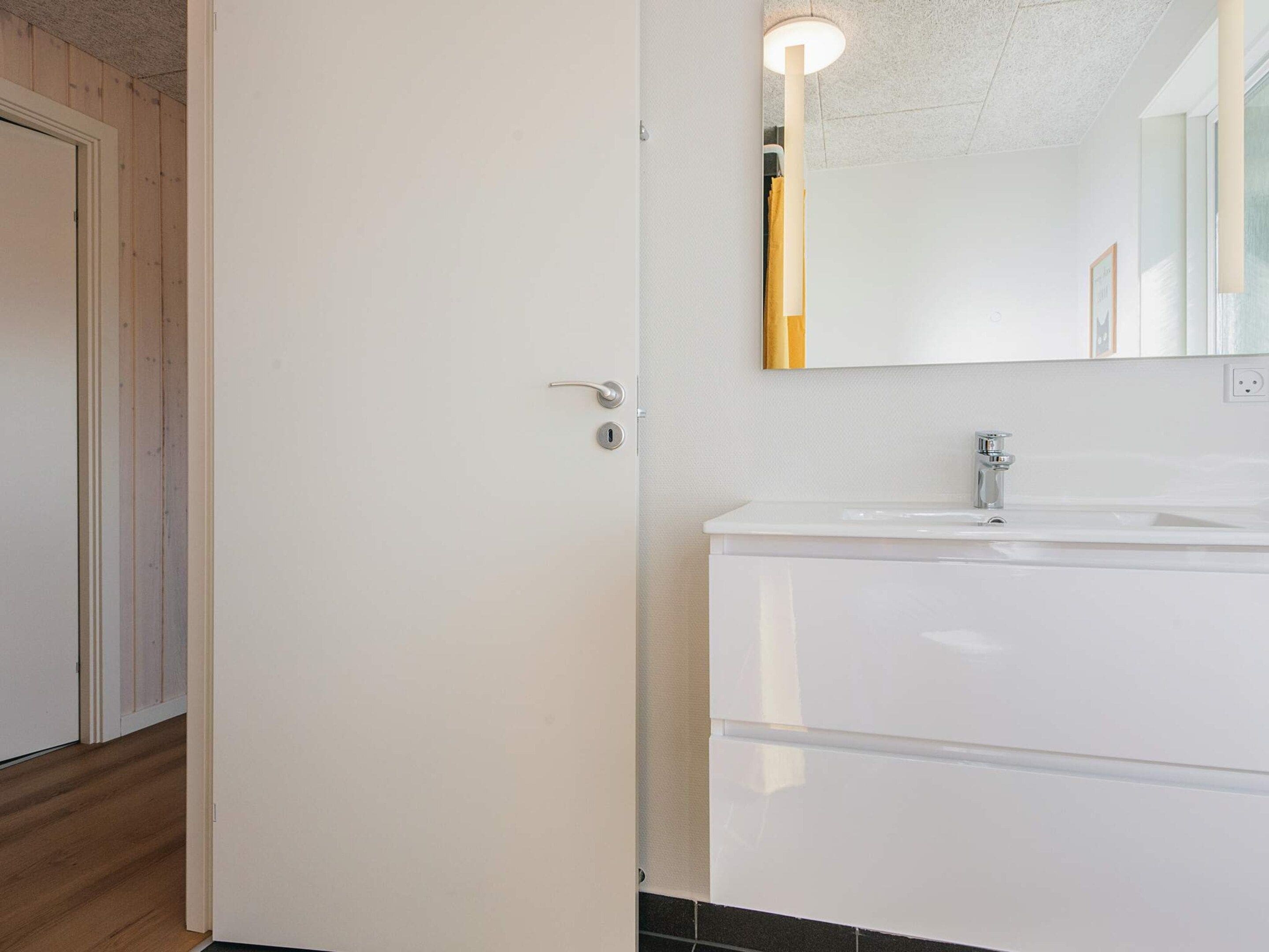 Un bany amb un lavabo blanc, un mirall i una porta.