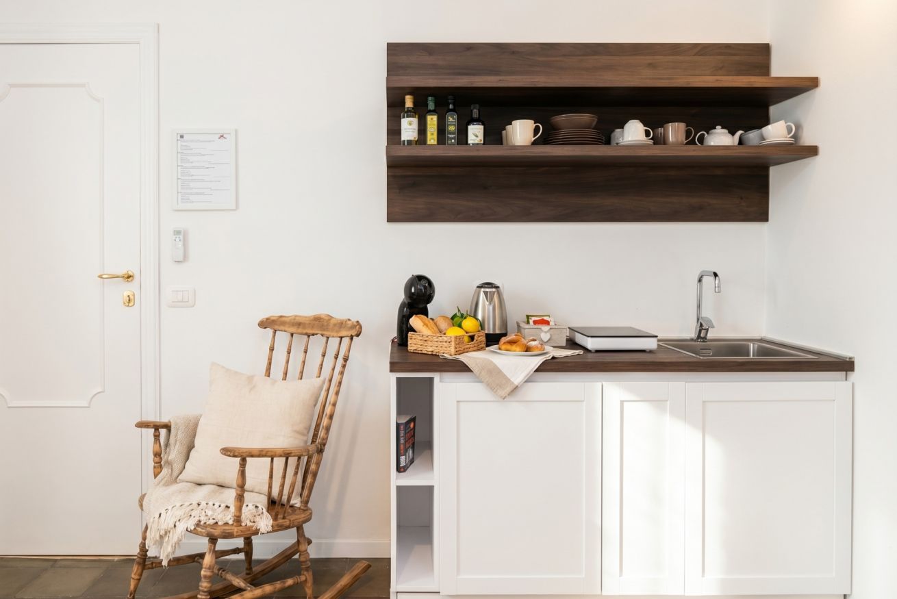 A kitchen with white cabinets, a wooden shelf with kitchenware, a rocking chair, and a door with a lock.