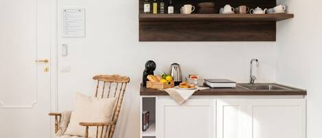 Una cocina con armarios blancos, un estante de madera con utensilios de cocina, un sillón mecedora y una puerta con cerradura.