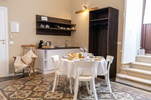 A dining area with a table set for four, a wooden rocking chair, a kitchen with a sink and shelves, and a staircase. - Tresca Charme - Suite 22-Suite with Private Terrace (Bari)