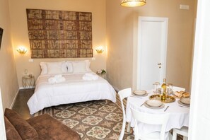 A hotel room with a bed, a dining table set for two, and a decorative wall piece.
