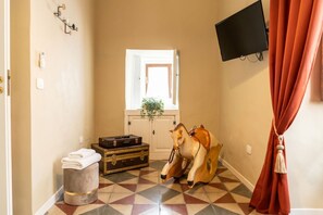 Een hal met een patroon vloer, een houten paardbeeld, een koffer en een aan de muur bevestigde televisie.