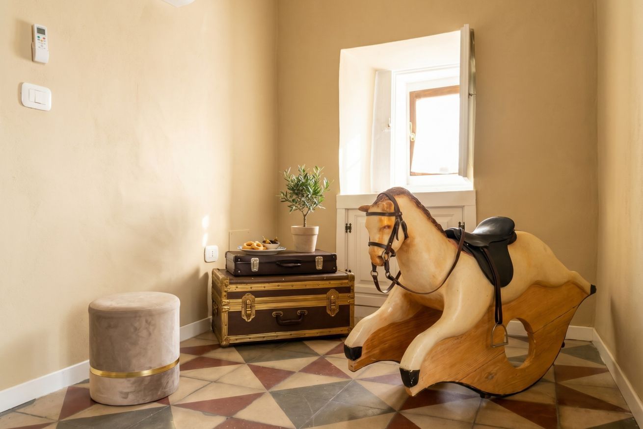 Un couloir avec un sol à motifs, un cheval à bascule en bois, un petit tabouret et une plante en pot.
