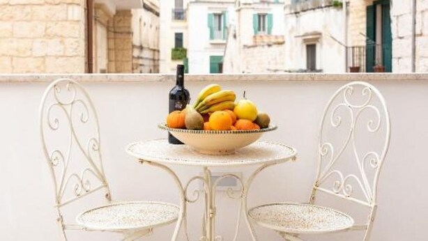 A balcony with a white metal table and chairs, a bowl of fruit, and a bottle of wine. - Tresca Charme - Suite 22-Suite with Private Terrace (Bari)