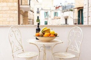 A balcony with a white metal table and chairs, a bowl of fruit, and a bottle of wine.