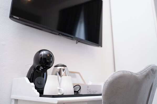 Ein Hotelzimmer mit Flachbildfernseher an der Wand, einer Kaffeemaschine und einem bequemen Sessel.