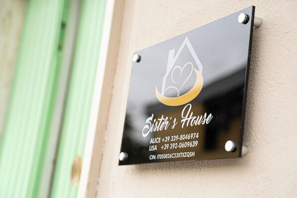 A black sign with white text and a gold heart symbol, indicating a business name and contact information. - Sister's House (Pisa)