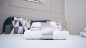 A neatly made bed with rolled white towels and a silver ribbon, a geometric patterned pillow, and a framed abstract painting on the wall. - Sister's House (Pisa)
