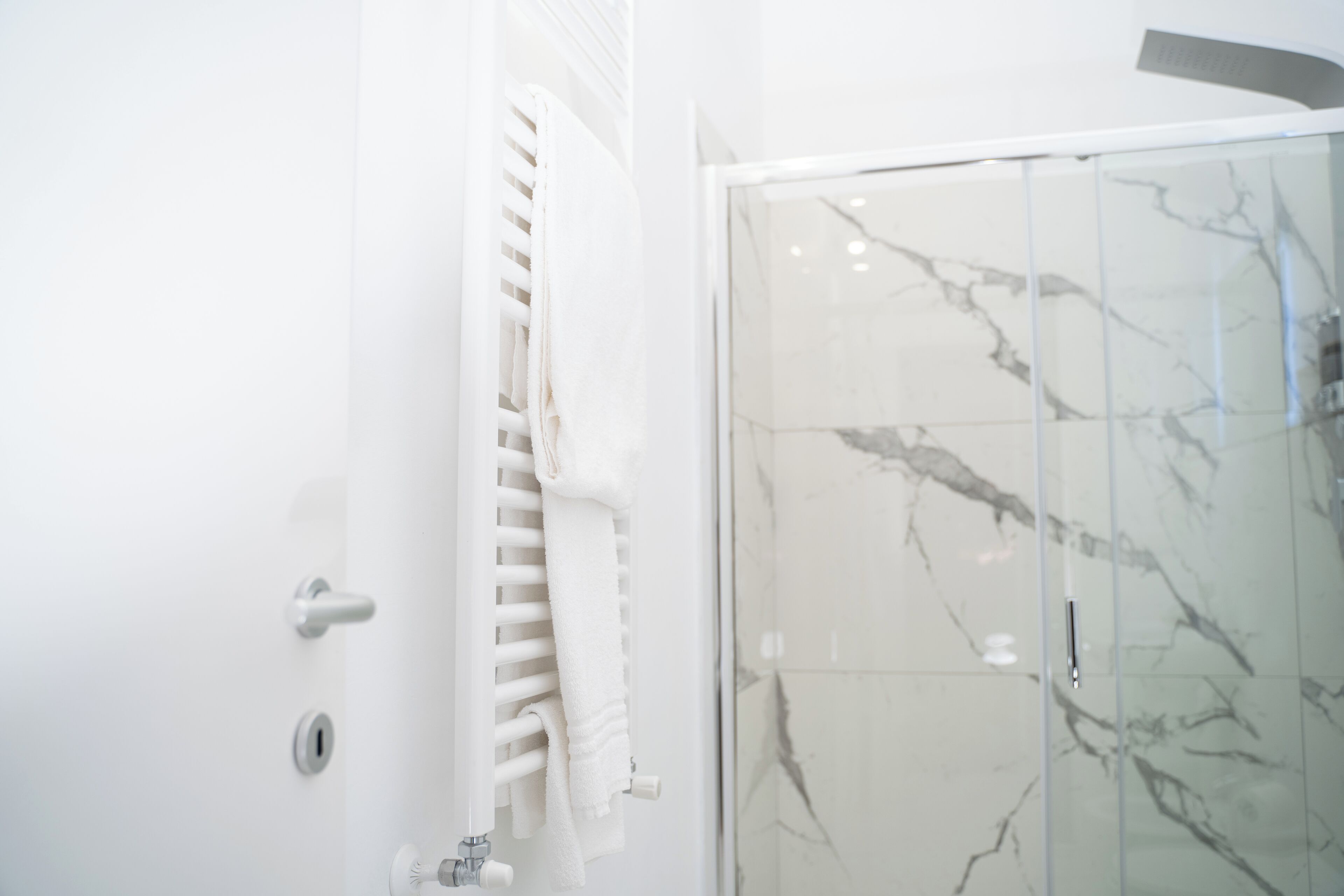 A bathroom with a glass shower enclosure, white tiled walls, and a towel rack.
