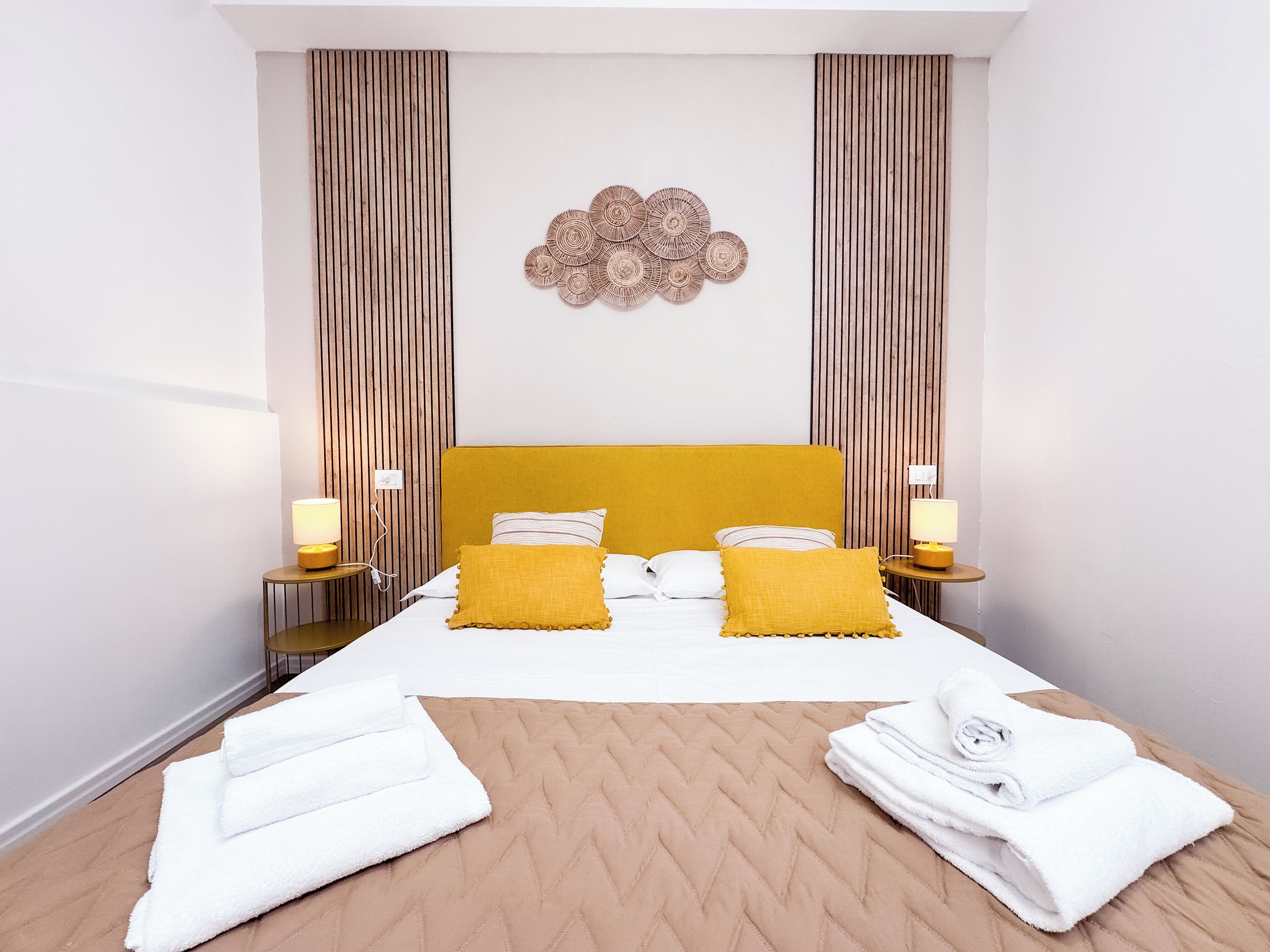 Une chambre d’hôtel avec un grand lit, deux tables de chevet avec des lampes, un élément décoratif mural et un plancher en bois.