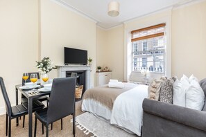Una camera d'albergo con un letto, un divano, una televisione, un tavolo da pranzo con sedie e una finestra con tende.