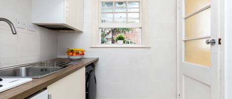 A compact kitchen with a built-in dishwasher, a window with a view of greenery, and a white door with a textured panel.