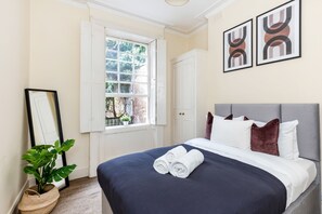 Un letto rifatto con una coperta blu scuro e cuscini bianchi, una pianta in vaso e due opere d'arte astratte alle pareti.