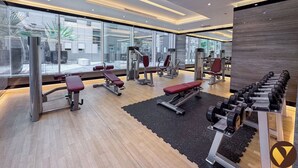Ett modernt gym med olika typer av träningsutrustning, stora fönster och ett trägolv.