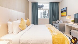 Ett hotellrum med en säng, ett skrivbord, en stol, en tv och ett fönster med gardiner.