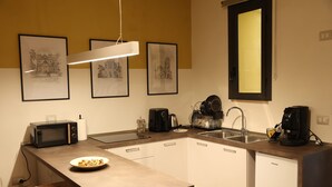 A compact kitchen with a microwave, coffee maker, and sink. There are framed pictures on the wall and a bench at the table. - Cimabue Cave Holiday House Caserta a stone's throw from the Royal Palace (Caserta)