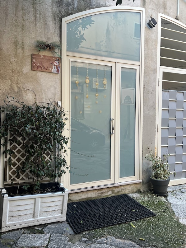 A building entrance with a glass door, a small potted plant, and a decorative sign.