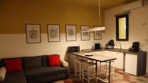 A compact living space with a kitchenette, a sofa with red cushions, and a patterned floor. - Cimabue Cave Holiday House Caserta a stone's throw from the Royal Palace (Caserta)