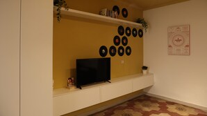 A living room with a TV on a white cabinet, a shelf with books and decorative items, and a wall with circular decorations. - Cimabue Cave Holiday House Caserta a stone's throw from the Royal Palace (Caserta)