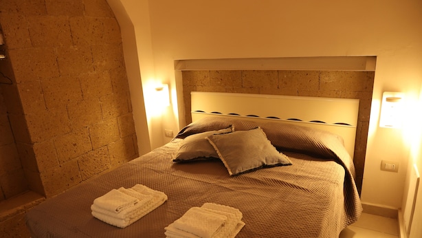 A neatly made bed with a brown bedspread and two pillows, two folded white towels on the bed, and two wall-mounted lights on either side. - Cimabue Cave Holiday House Caserta a stone's throw from the Royal Palace (Caserta)