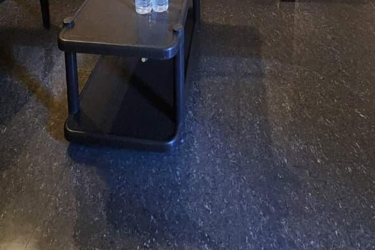 A hotel room with a bed, a small table with water bottles, a ceiling fan, and a bathroom visible in the background.