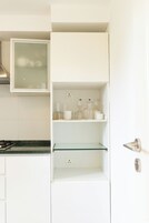 A kitchen with white cabinets, a glass shelf, and a microwave.