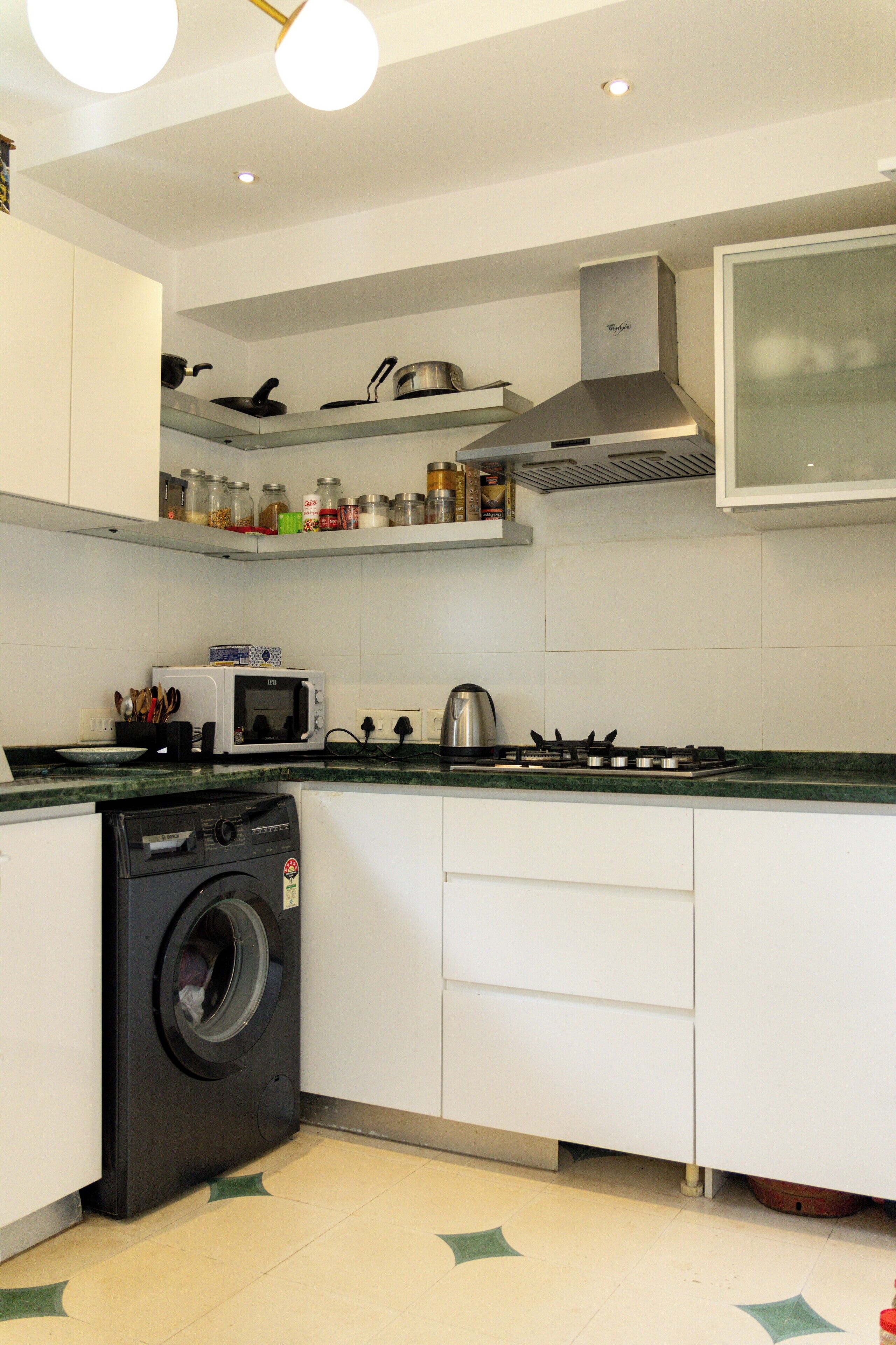 Una cocina compacta con lavadora, microondas, cocina y diversos utensilios de cocina en estantes.