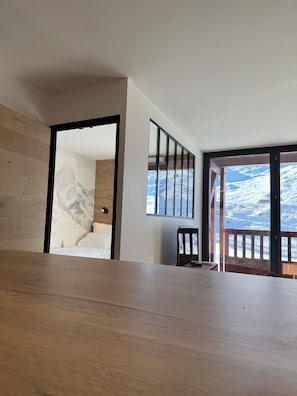 A room with a wooden floor, a bed with white bedding, a mountain mural on the wall, and a large window with a snowy view. - Premium Ski-in/Ski-out Apartment with Panoramic View | Montana 1st Floor (Les Belleville)
