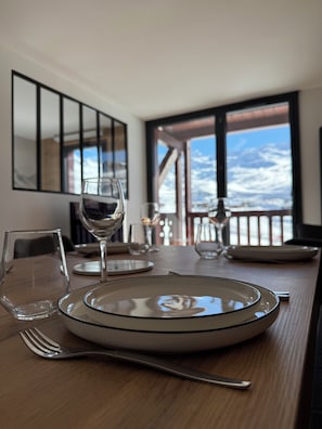 A dining table set with plates, glasses, and cutlery, with a view of a snowy landscape through large windows. - Premium Ski-in/Ski-out Apartment with Panoramic View | Montana 1st Floor (Les Belleville)