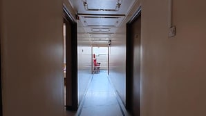 A long, narrow hotel corridor with a red chair at the end, a staircase, and a door on the right. - Fabhotel Ramesh Inn (Rajgurunagar)