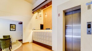 A reception area with a wooden reception desk, a wall-mounted telephone, and a large elevator. - Fabhotel Holiday Park (Thalassery)