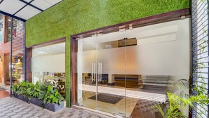A modern building with a green wall and large glass doors, leading to an interior with a tiled floor and a fireplace. - Fabhotel Holiday Park (Thalassery)