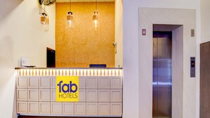 A hotel reception desk with a 'fab hotels' sign, an elevator, and a wall-mounted light fixture. - Fabhotel Holiday Park (Thalassery)