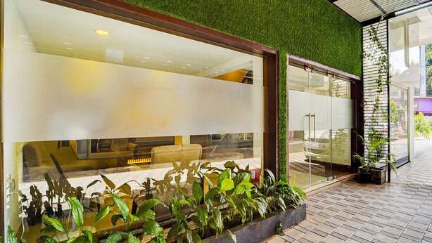 A modern building with large glass windows, a green artificial grass roof, and potted plants in front. - Fabhotel Holiday Park (Thalassery)