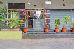 Une devanture de magasin ornée de plantes en pot, une porte à volets fermés et un panneau indiquant la présence d’un ascenseur.