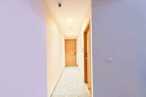 A narrow hallway with a wooden door at the end, a light switch on the wall, and a ceiling light. - Fabhotel Elbeso (Dera Bassi)