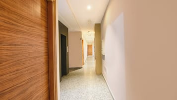 A hallway with a wooden door on the left, a dark door in the middle, and a light switch on the right.
