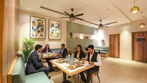 A modern dining area with a long table, ceiling fans, and abstract art on the walls. - Fabhotel Elbeso (Dera Bassi)